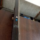 Fotografie zachycuje hmatník a krk strunového nástroje tmavé barvy, pravděpodobně z dřeva. Na krku jsou umístěny dva ladicí kolíky, jeden bílý a jede…