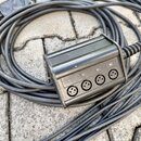Černý rozdělovač kabelů z plastu s čtyřmi konektory XLR. Nad každým konektorem je bílý nápis: 01., 02., 03. a 04. Povrch plastového krytu vykazuje dr…