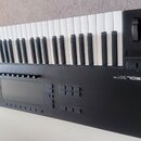 Černý MIDI kontrolér s klaviaturní klávesou. Na pravé straně je nápis KONTROL S61 MK2, dvě otočné voliče a několik tlačítek. V horní části jsou bílé…