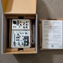 Bílá mixovací konzole značky YAMAHA, model AG03, umístěná v originální hnědé kartonové krabici. Vedle konzole je srolovaný bílý kabel a papírová doku…
