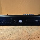 Zadní strana černého elektronického zařízení v kovovém šasi. Na zadním panelu jsou konektory s popisky POWER, 12VDC (input) 2000mA, EXP 1, EXP 2, DMX…