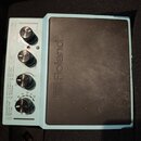 Světle modrý elektronický bicí pad s černou gumovou dopadovou plochou. Na přístroji je nápis Roland a označení SP-LONE ELECTRONIC PAD. V levé části j…
