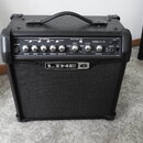 Černý kytarový kombo zesilovač s látkovou mřížkou a nápisem LINE 6. Na ovládacím panelu jsou knofíky s popisky DRIVE, BASS, MID, TREBLE, CHAN VOL a M…