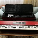 Červený digitální klavír s bílými a černými klávesami. Na pravé straně je nápis nord piano, v horní části se nachází ovládací panel s tlačítky a posu…
