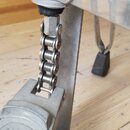 Detailní záběr na kovový mechanismus pedálu, pravděpodobně basového pedálu. Je vidět řetězové spojení s kovovými články a stříbrný šlapadlo s reliéfn…