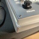 Detailní pohled na roh stříbrného efektpedálu s kovovým povrchem. Na horní desce je viditelný černý otočný knoflík s nápisem VOLUME a přepínač s ozna…