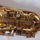 Detailní pohled na zlatý lakovaný saxofon. Jsou vidět klapy s bílými polštáři a červené plfeltové podložky u mechanismů. Povrch nástroje je lesklý, b…