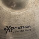 Detailní záběr na povrch činchy v bronzové barvě s viditelným obrušováním. Na povrchu je černý nápis „eXpression“ a pod ním text „13"/33cm Regular Hi…