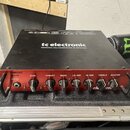 Černý basový zesilovač s červeným předním panelem. Na horní části je bílý nápis tc electronic a text DESIGNED AND ENGINEERED IN DENMARK. Na předním p…