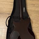 Tmavě hnědá elektrická kytara s lesklým povrchem položená na černém softcasu. Na zadní straně krku je svisle napsáno YAMAHA s doprovodným logem. Na z…
