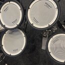 Fotografie zachycuje čtyři bílé pady elektronické bicí s černými gumovými okraji. Na každém padu je nápis „Roland“ s doprovodným textem „Reg. U.S. Pa…