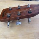 Detail hlavy akustické kytary z tmavého dřeva s kovovými ladičkami. Na dřevě je vyryt nápis Sigma Guitars a pod ním menší označení EL-200. Povrch vyk…