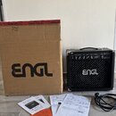Na fotografii je černý kytarový kombozesilovač s logem ENGL na mřížce reproduktoru a nápisem Gy Master 15 v pravém horním rohu. Vedle zesilovače stoj…