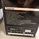 Fotografie zachycuje část černé krabice s bílým textem v sekci Features:, která vyjmenovává technické parametry zařízení. V dolní části je vidět nápi…