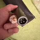 Fotografie zachicuje ruku držící černý kabel s konektorem typu XLR. V konektoru jsou vidět tři kovové piny. Vedle konektoru je v prstech držena malá…