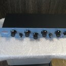 Modrý rackový ekvalizér s černým šasi a ovládacími knoflíky. Na levé straně je bílý nápis WARM AUDIO a pod ním text PROGRAMMABLE TUBE EQ-WA. Přední p…