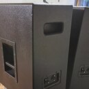 Dvě černé reproduktorové bedny s texturovaným povrchem. Každá bedna má na boku úchopovou rukojeť a v dolní části panel s dvěma konektory. Na přední s…