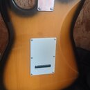 Zadní strana elektrické kytary s tělem v žlutomodrém sunburst provedení. Na zadní straně jsou dva kovové kryty s viditelnými šrouby, jeden u krku a d…