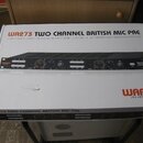 Bílá papírová krabice s nápisy „WA273 TWO CHANNEL BRITISH MIC PRE“ a logem „WARM AUDIO“. Na horní straně je fotografie černého rackového zařízení s o…