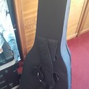 Černý polštovovaný pouzdro (gig bag) na hudební nástroj. Na zadní straně jsou vidět nastavitelné ramenní popruhy a spodní úchytky. Povrch materiálu v…