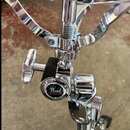 Detail chromovaného mechanismu bubnového stojanu. Na kulatém prvku je viditelné logo Pearl a nápis HYDRO-LOCK SYSTEM. Povrch vykazuje mírné znečištěn…