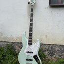 Světle zelená elektrická basová kytara s bílým perleťovým pickguardem. Na hlavě nástroje je viditelné logo "Squier". Tělo kytary má v dolní části čer…