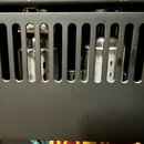 Šedý kovový panel s dvanácti svislými oválnými otvory. V některých otvorech jsou vidět bílé a kovové součástky, z nichž jedna nese neúplný nápis „CMS…