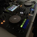 Černý DJ 컨트롤러 s dvěma jogovými koly a centrálním mixážním sekcí. Na displeji je viditelný nápis rekordbox 6. V pravé části je uveden nápis Pioneer DJ…