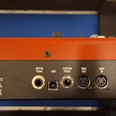 Záběr na zadní panel hudebního přístroje v oranžovo-černé barvě. Jsou zde viditelné konektory s popisky ROTOR PEDAL, USB, SUSTAIN PEDAL, MIDI OUT a M…