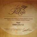 Oválná papírová štítka nalepená na dřevěném povrchu. Obsahuje nápisy „La Patrie“, „Handmade in the Village of LaPatrie Québec Canada. / Fait à la mai…