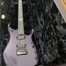 Fialová elektrická kytara s dvoma humbuckery a jedním single-coil snímačem, umístěná v černém plišovém kufru. Na hlavě hmatníku je viditelné logo "Ib…