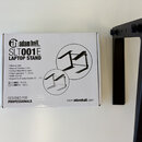 Na fotografii je bílá kartonová krabice a vedle ní černý kovový stojan. Na krabici je nápis „adam hall events“, model „SLT001E LAPTOP STAND“ a text „…