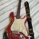 Elektrická kytara typu Stratocaster s červeným lakem, který je výrazně odřený a v mnoha místech chybí, čímž odhaluje dřevěný povrch korpusu. Nástroj…