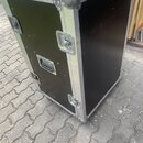Černý transportní case s hliníkovými hranami a kovovými rohy. Na přední straně jsou umístěny tři kovové zámky a jedna plastová rukojeť. Povrch vykazu…