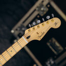 Hlava elektrické kytary s přírodním dřevěným povrchem a šesti ladicími kolíky v šedé barvě. Na hlavě je černý nápis Fender a STRATOCASTER, vpravo se…