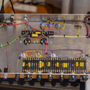 Fotografie zachycuje vnitřek kovového šasi s elektronickými součástmi a rozvody kabelů. V dolní části je umístěna řada odporů a kondenzátorů, z nichž…
