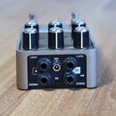 Stříbrný efekt pedál s třemi černými oválnými ovladači s kovovými knoflíky. Na zadní straně jsou nápisy 1/MONO, 2/STEREO, IN, OUT, USB a 9VDC s označ…