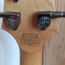 Zadní strana hlavy kytary z přírodního dřeva s kovovými ladičkami. Na zadní straně je nápis WI20080371 a pod ním text Crafted in Indonesia. Nad tímto…
