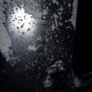 Detailní záběr na tmavý, kovový povrch s výraznou korozí a odsloupavým lakem. Povrch je pokrytý světlými skvrnami a oxidací. V uprostřed jsou vidět z…