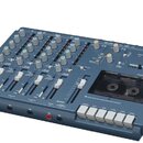 Modrý vícesledový magnetofon s integrovaným mixážním pultem. Na přístroji je v pravém horním rohu nápis TASCAM a níže označení PORTASTUDIO 414 SL. Za…