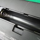 Detail otevřeného bateriového prostoru černého plastového přístroje. Uvnitř je vidět kovová pružina a štítek. Na bílém štítku je nápis CASIO®, RATING…