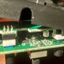 Fotografie zachycuje vnitřek elektronického zařízení s černým plastovým krytem, který je mírně nadzdvihnutý. Uvnitř jsou vidět dvě zelené desky plošn…