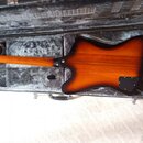 V otevřeném černém kufru s šedým vnitřkem leží kytara s tělem v barvě sunburst. Je vidět zadní strana hředu a těla nástroje z dřeva s viditelnou masi…