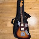Elektrická kytara s trupem v barevnosti sunburst a hnědým hmatníkem, umístěná v černém softcasu. Na hlavě je viditelné logo Fender JAPAN. Kytara má t…