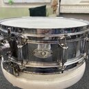 Chromovaná bubnová sada s bílým obsahem. Na korpusu je oválný štítek s nápisy DYNA-SONIC, SERIAL NO. 7491 a CUSTOM BUILT. Povrch chromu vykazuje znám…