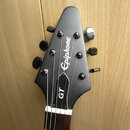 Fotografie zachycuje hlavu černé elektrické kytary. Na povrchu je bílý nápis Epiphone a pod ním vertikálně umístěný nápis GT. Nástroj má šest ladicíc…