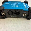Modrý elektronický přístroj s černým plastovým rámem a nápisy SAMSON a S-monitor. Na zadní straně jsou konektory s popisky THRU, MIC IN, MIC THRU a S…