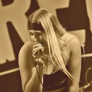 Fotografie zachicuje zpěvačku s mikrofonem v ruce. Mikrofon je kovový, stříbrné barvy a připojen k kabelu. Na snímku nejsou viditelné žádné značky an…