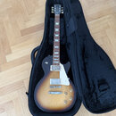 Elektrická kytara s trupem v barevnosti sunburst a tmavým hmatníkem, umístěná v černém měkkém pouzdře. Na hlavě nástroje je viditelné logo Gibson. Ky…