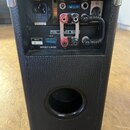 Zadní strana černého komba s povrchem z texturovaného vinylu a kovovými rohy. Na zadním panelu jsou nápisy AC INPUT, DC INPUT, FUSE 15A a PRE AMP OUT…